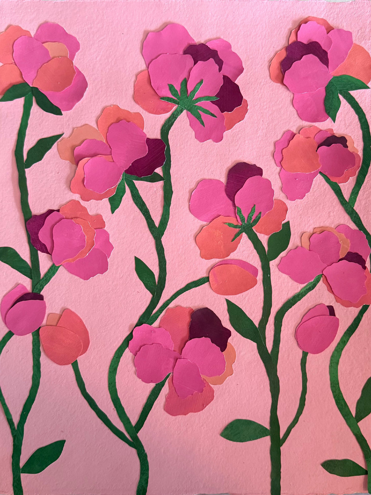 Pink artwork on painted paper featuring layered pink flowers with green stems and leaves, displayed against a light gray wall.